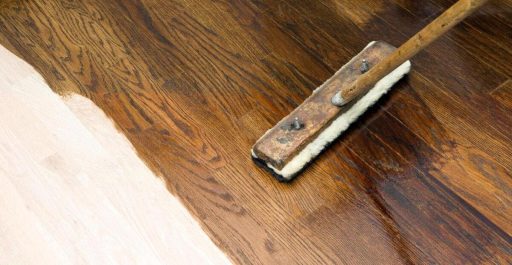 Applying dark stain to hardwood floor showing the contrast between bare sanded wood and the finished darker color
