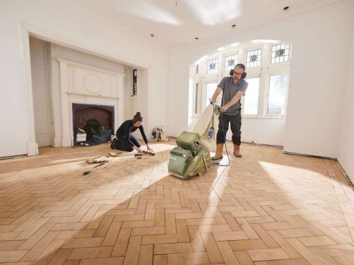 Professional hardwood floor sanding with dust control equipment during a full refinishing project in a large room