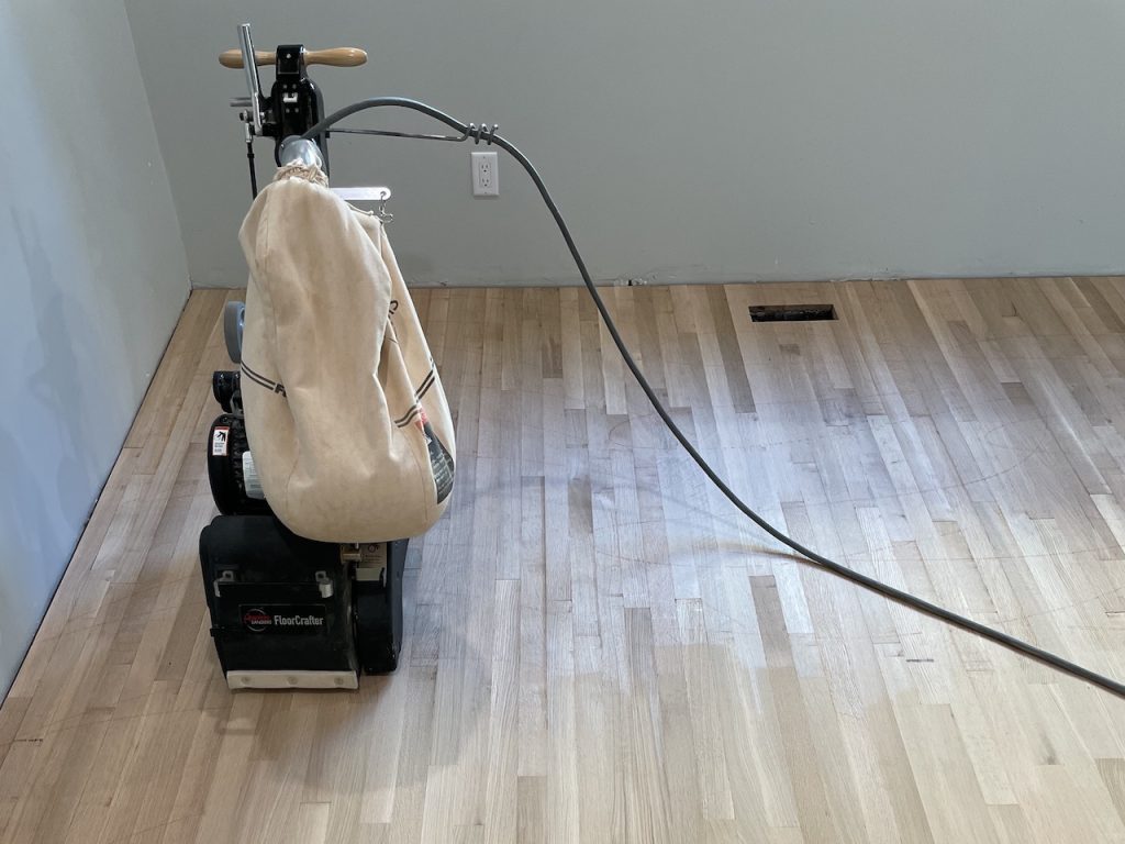 Hardwood floor sanding machine on thick floorboards showing the kind of surface material that affects refinishing potential and long-term durability
