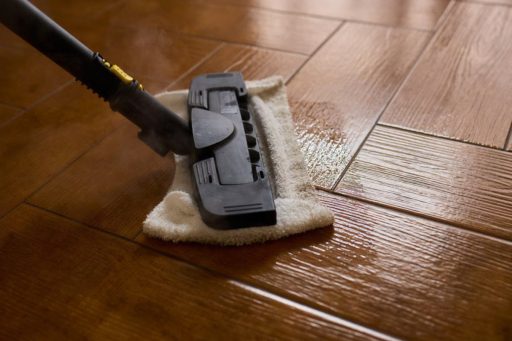 Steam mop cleaning hardwood floor showing direct heat and moisture exposure across the wood surface
