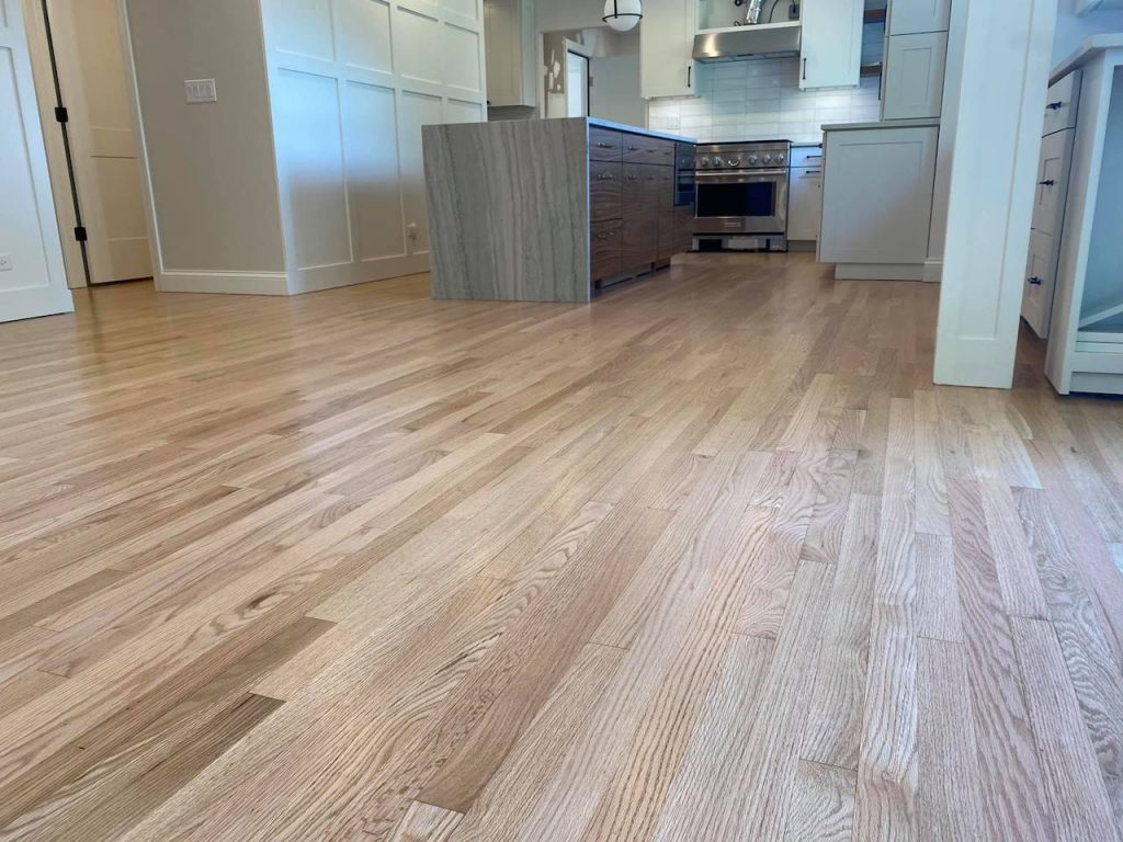Refinished hardwood floor in open kitchen showing a clean renewed surface across a larger layout that affects total project cost