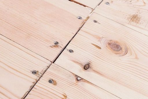 Large gaps and visible holes in hardwood floor boards before repair filling and refinishing
