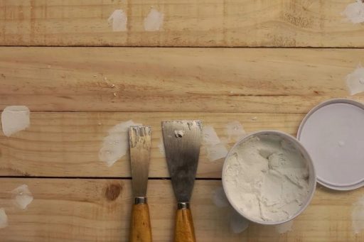 Wood filler and putty knives used to repair holes in hardwood floor before sanding and refinishing