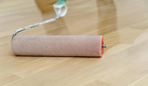 Applying a fresh finish coat to hardwood floor during a buff and coat restoration process