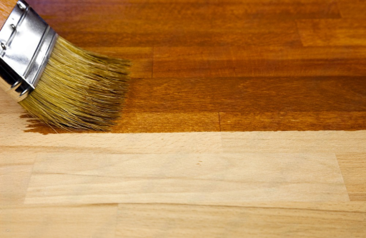 Applying wood stain to a hardwood floor showing natural wood before and after staining
