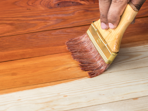 Applying wood stain to hardwood floor with brush to deepen color and highlight the natural grain