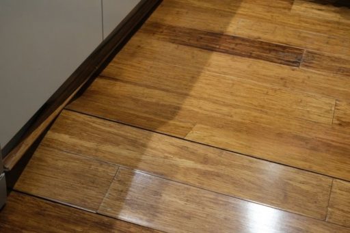 Moisture-damaged hardwood floor boards with visible staining and uneven tone