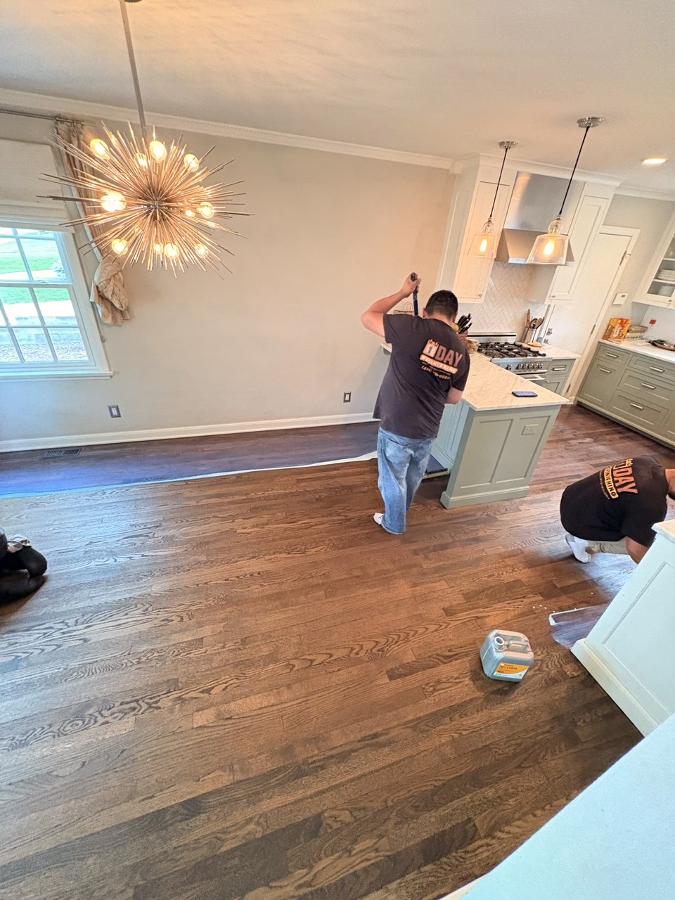 1 DAY Refinishing crew working on hardwood floor refinishing and staining in open kitchen and living space
