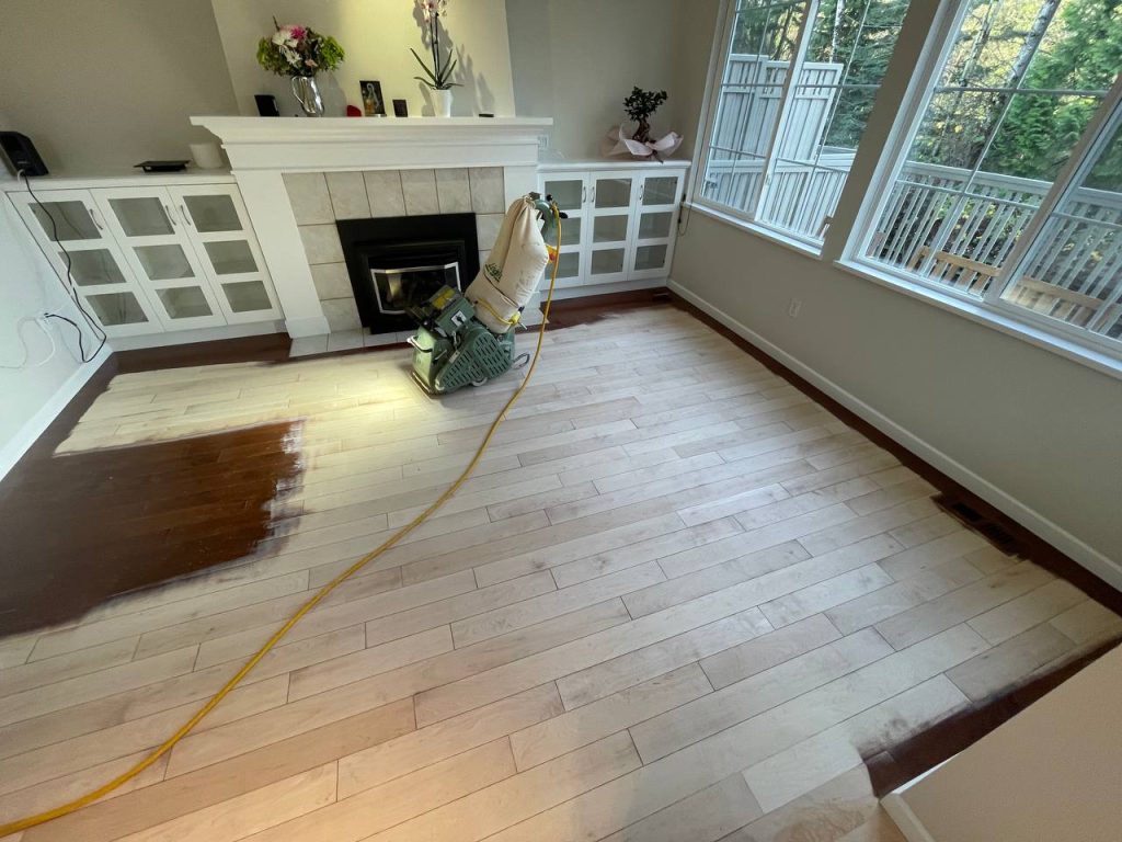 Hardwood floor refinishing in a bright living room with sanding and stain testing in progress