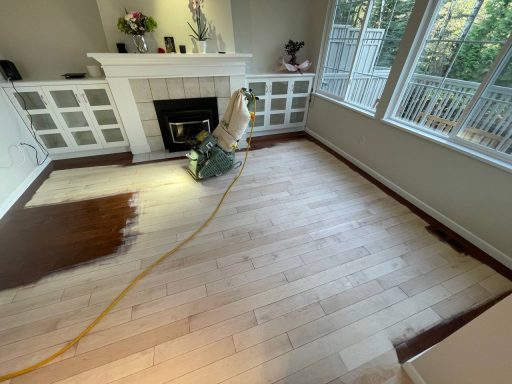 Hardwood floor refinishing in a bright living room with sanding and stain testing in progress