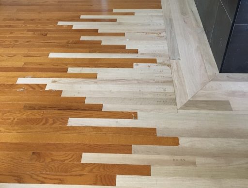 Hardwood floor restoration showing sections sanded to bare wood where full refinishing is required instead of a buff and coat