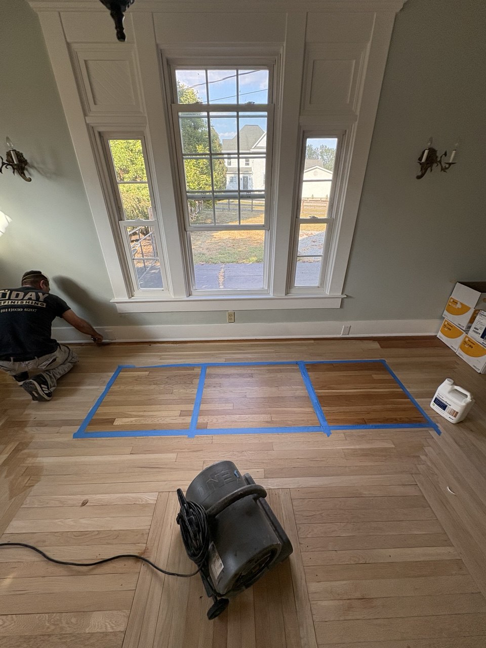 Hardwood floor stain sample testing in progress with color sections taped off for comparison