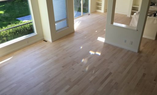 Large room with hardwood floors before refinishing showing project size and overall floor condition
