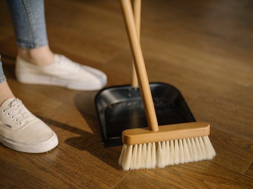 Sweeping hardwood floor with a soft broom to remove dust and debris